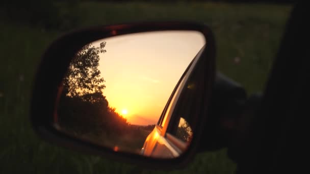 Een prachtige zonsondergang wordt weerspiegeld in de spiegel van de auto. het concept van avontuur en reizen. reizen met de auto buiten de stad. familie reis naar de natuur in een weekend - Video