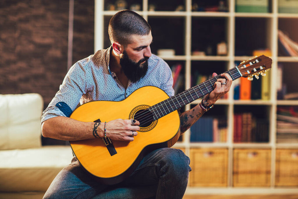 Красивий молодий бородатий чоловік у сорочці грає на класичній гітарі
.  - Фото, зображення
