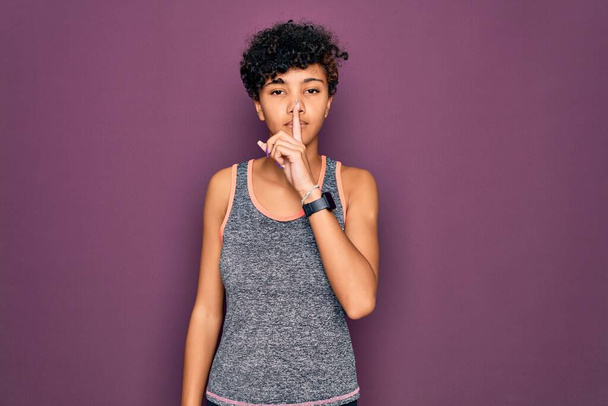 A fiatal, gyönyörű afro-amerikai afro sportos nő sportruhát visel, és arra kér, hogy hallgasson ujjal az ajkain. Csend és titkos koncepció. - Fotó, kép