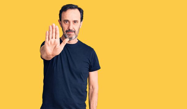 Middle age handsome man wearing casual t-shirt doing stop sing with palm of the hand. warning expression with negative and serious gesture on the face.  - Photo, Image