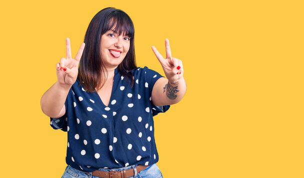 Young plus size woman wearing casual clothes smiling with tongue out showing fingers of both hands doing victory sign. number two.  - Photo, Image