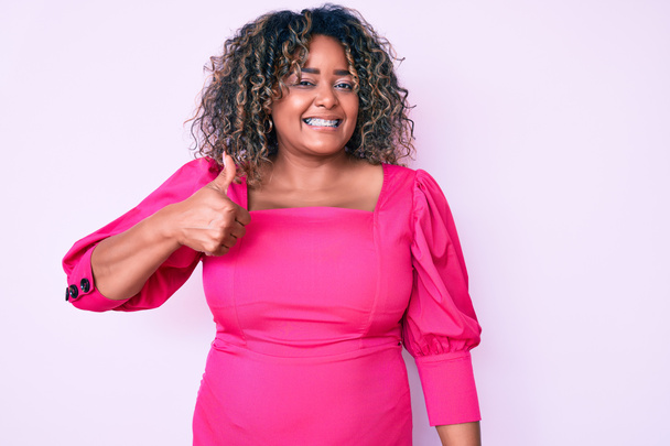 Young african american plus size woman wearing casual clothes smiling happy and positive, thumb up doing excellent and approval sign  - Photo, Image