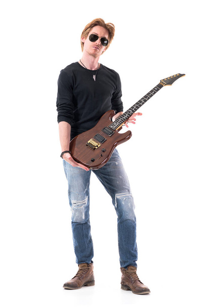 Guapo rockero elegante sosteniendo su guitarra eléctrica mirando a la cámara. Retrato de cuerpo entero aislado sobre fondo blanco
.  - Foto, imagen