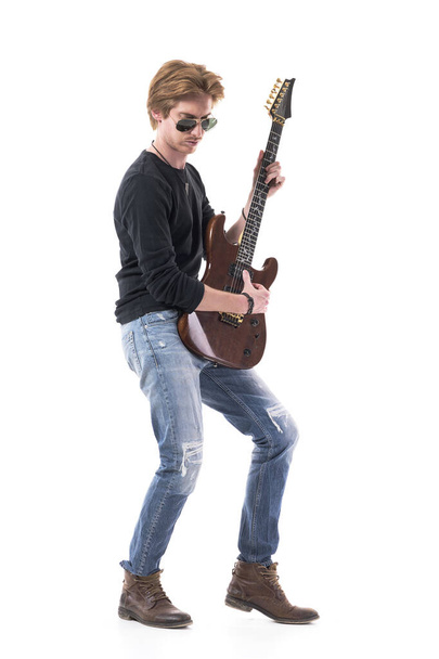 Vista lateral de rockero de pelo rojo tocando guitarra eléctrica con gafas de sol mirando hacia abajo. Retrato de cuerpo entero aislado sobre fondo blanco
.  - Foto, Imagen