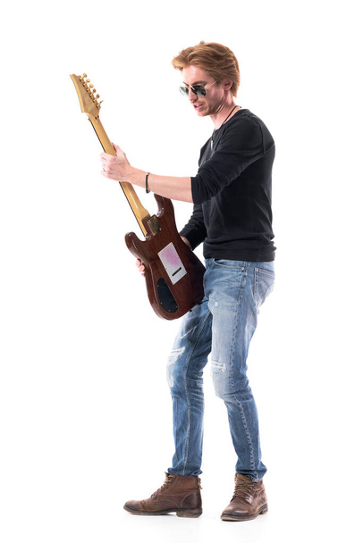 Вид збоку на талановитого пристрасного рок-н-рольного гітариста, який грає на електрогітарі. Портрет повної довжини ізольований на білому тлі
.  - Фото, зображення