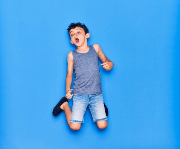 Adorable enfant portant des vêtements décontractés sautant sur fond bleu isolé - Photo, image