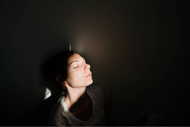 Girl sitting alone in sunlight pocket in dark room. mental health concept - Photo, image