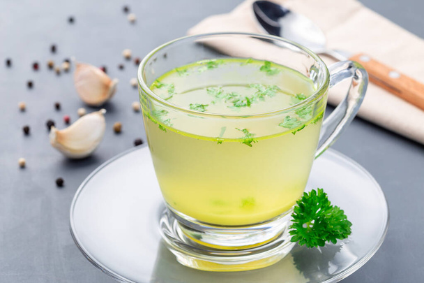 Homemade chicken broth in a glass cup garnished with chopped parsley, horizontal - Fotoğraf, Görsel