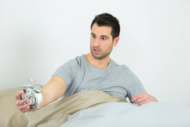 shocked man in bed holding alarm clock - Foto, Imagem