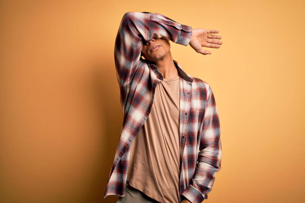 Young handsome african american man wearing casual shirt standing over yellow background covering eyes with arm, looking serious and sad. Sightless, hiding and rejection concept - Fotó, kép