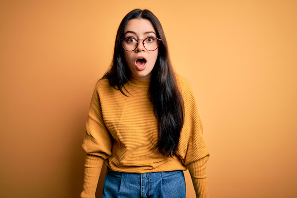 Mladá brunetka žena nosí brýle a ležérní svetr přes žluté izolované pozadí strach a šokován překvapením a užaslý výraz, strach a vzrušený obličej. - Fotografie, Obrázek