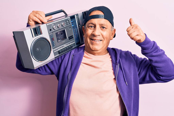 Senior pohledný šedovlasý moderní muž poslouchající hudbu pomocí vintage boombox usměvavý šťastný a pozitivní, palec nahoru dělá vynikající a schvalovací znamení - Fotografie, Obrázek