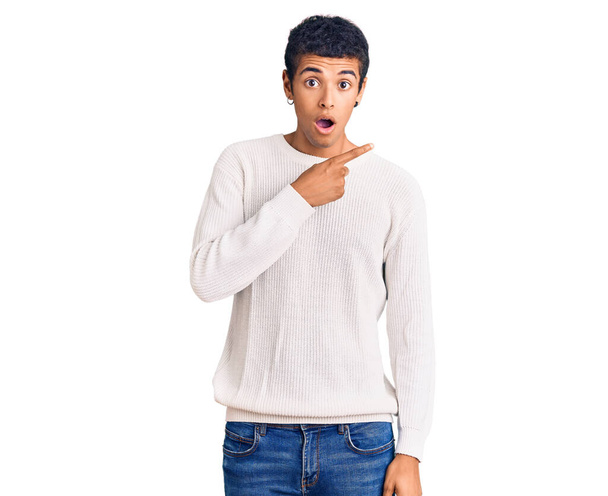 Giovane uomo africano amercian indossa abiti casual sorpreso indicando con il dito di lato, bocca aperta espressione stupita.  - Foto, immagini