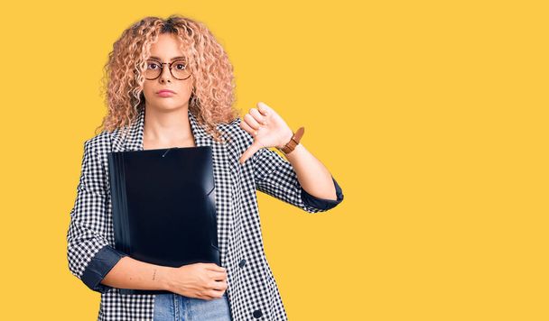 Young blonde woman with curly hair holding business folder with angry face, negative sign showing dislike with thumbs down, rejection concept  - Photo, Image