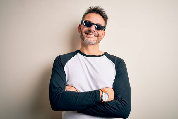 Jonge knappe man draagt grappige schurk leven zonnebril meme over witte achtergrond gelukkig gezicht glimlachen met gekruiste armen kijken naar de camera. Positief persoon. - Foto, afbeelding