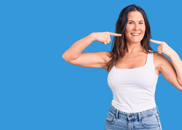 Young beautiful brunette woman wearing casual sleeveless t-shirt smiling cheerful showing and pointing with fingers teeth and mouth. dental health concept.  - Photo, Image