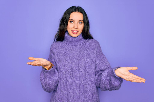 Young beautiful woman wearing casual turtleneck sweater standing over purple background smiling cheerful with open arms as friendly welcome, positive and confident greetings - Photo, Image