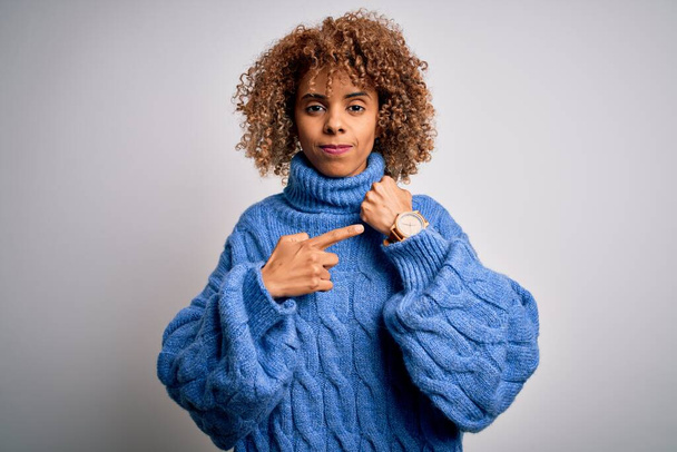 Young beautiful african american woman wearing turtleneck sweater over white background In hurry pointing to watch time, impatience, looking at the camera with relaxed expression - Photo, Image