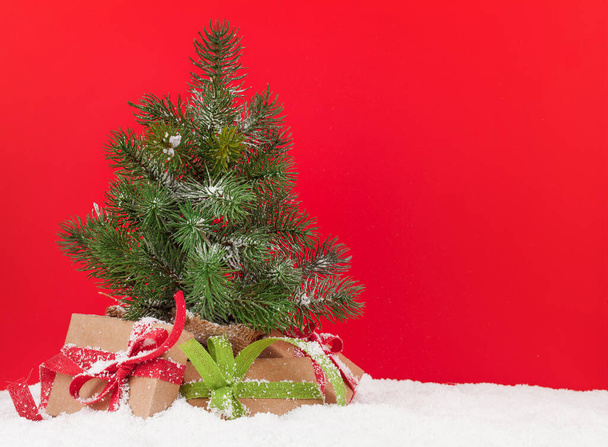 Christmas greeting card with small fir tree and gift boxes in front of red background and copy space for your xmas greetings - Photo, Image
