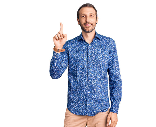 Mladý pohledný muž na sobě ležérní oblečení ukazuje a ukazuje prstem číslo jedna a zároveň se usmívá sebevědomě a šťastně.  - Fotografie, Obrázek
