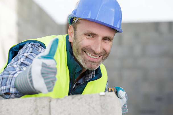 portrait of a cheerful male builder showing thumbs up - Fotografie, Obrázek