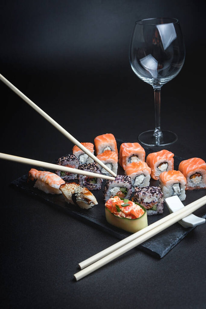 Sushi with red wine on a dark restaurant background. Chopsticks. A glass of wine. Soy sauce. Rolls and sushi. Japanese cuisine. - 写真・画像