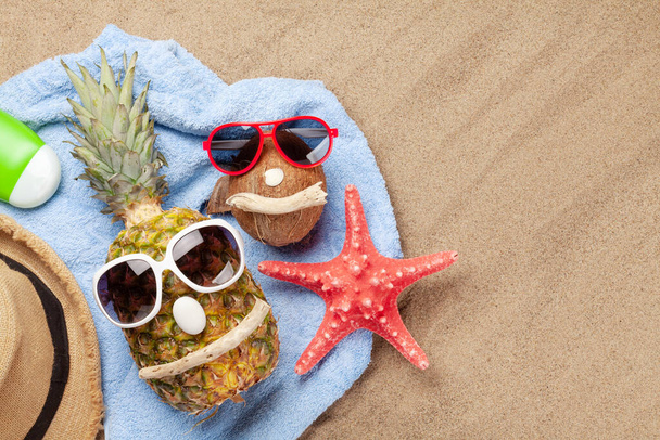 Reife Ananas und Kokosnuss mit Sonnenbrille über Sandhintergrund mit Kopierraum. Reise- und Urlaubskonzept. Draufsicht flach gelegt - Foto, Bild