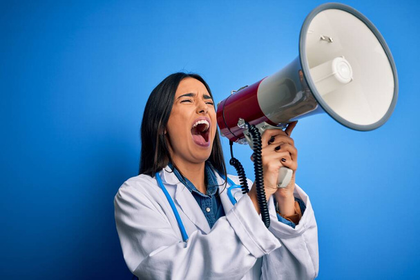 Die hispanische Ärztin im weißen Arztkittel schreit wütend aus Protest per Megafon. Aufgeregt schreien auf Lautsprecherdurchsagen und Schreinachrichten - Foto, Bild