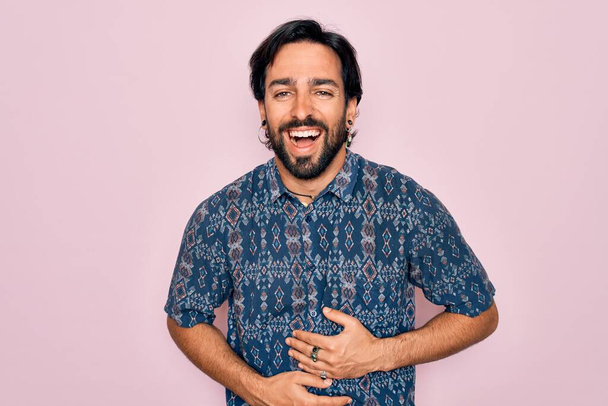 Junge gut aussehende hispanische Bohème Mann trägt Hippie-Stil über rosa Hintergrund lächelnd und laut lachen, weil lustig verrückten Witz mit den Händen auf dem Körper. - Foto, Bild