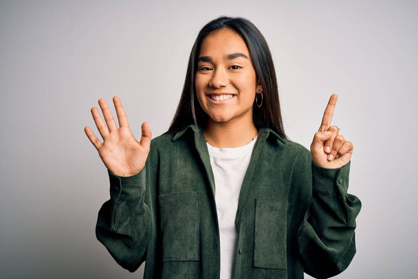 Jonge mooie aziatische vrouw dragen casual shirt staan over geïsoleerde witte achtergrond tonen en wijzen met vingers nummer zes terwijl glimlachen zelfverzekerd en gelukkig. - Foto, afbeelding