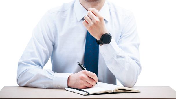 Um homem de negócios escreve com uma caneta em um caderno preto enquanto está sentado em uma mesa.O cara segura a cabeça. Relógio inteligente em uma mão
. - Foto, Imagem
