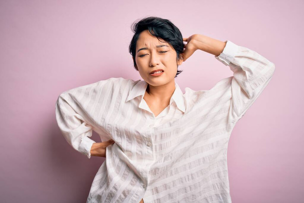 Young beautiful asian girl wearing casual shirt standing over isolated pink background stretching back, tired and relaxed, sleepy and yawning for early morning - Fotó, kép