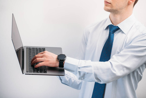 Un tipo con una camisa ligera con una corbata sobre un fondo blanco está escribiendo en un teclado portátil. Foto panorámica con el bekt principal desde la izquierda. Lugar para la inscripción - Foto, imagen