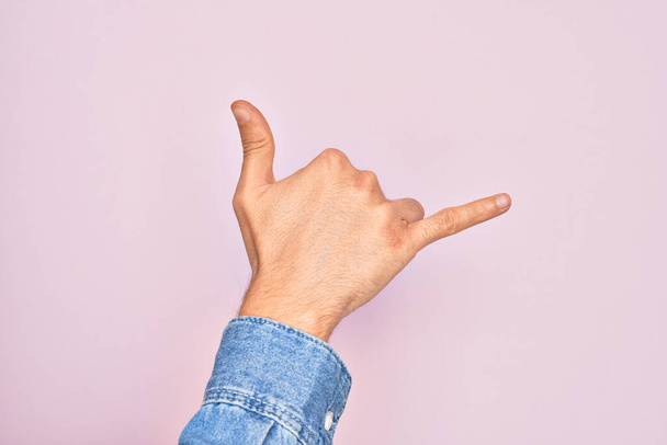 Mano de joven caucásico mostrando los dedos sobre el fondo rosa aislado gesto shaka hawaiano gesto de saludo, teléfono y símbolo de comunicación - Foto, Imagen