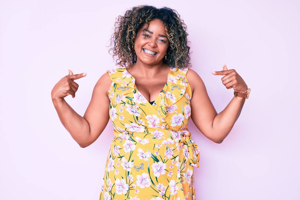 Young african american plus size woman wearing casual clothes looking confident with smile on face, pointing oneself with fingers proud and happy.  - Foto, Imagen
