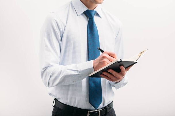The guy writes in a black notebook. A man on a white background with a blue tie in a white shirt. Note in the notebook. - Foto, Imagen