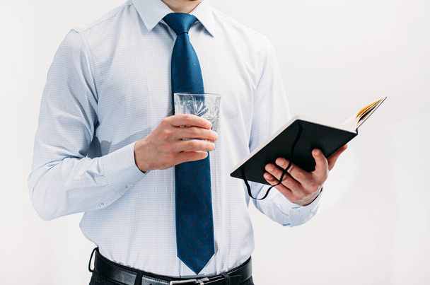 Хлопець у білій сорочці і блакитна краватка на білому тлі. Чоловік тримає склянку з коктейлем, а в його другій руці блокнот. Він дивиться на нотатки. Автор. Бізнесмен
. - Фото, зображення