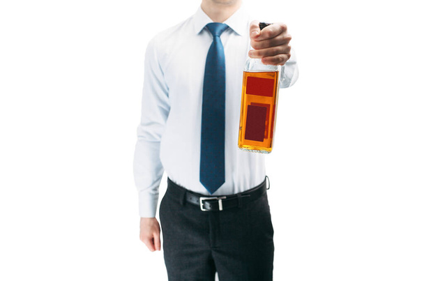 Egy fehér inges fickó kék nyakkendőben tart egy üveg whiskyt. Fehér háttér. A munkahelyi alkoholizmus izolálása. - Fotó, kép