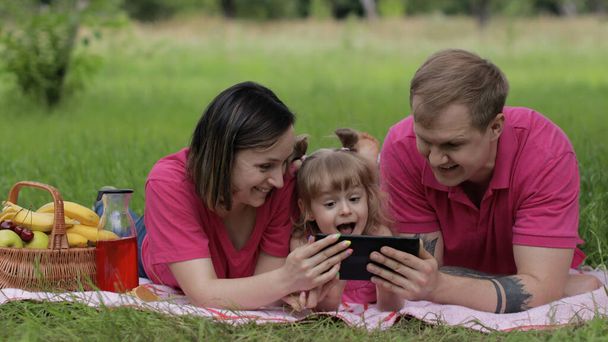 Сімейний пікнік на вихідні. Дочка дівчинка з матір'ю і батьком грають онлайн ігри на планшеті
 - Фото, зображення
