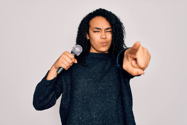 Junge afrikanisch-amerikanische Lockensängerin singt mit Mikrofon auf weißem Hintergrund und zeigt mit dem Finger in die Kamera und zu Ihnen, Handzeichen, positive und selbstbewusste Geste von vorne - Foto, Bild