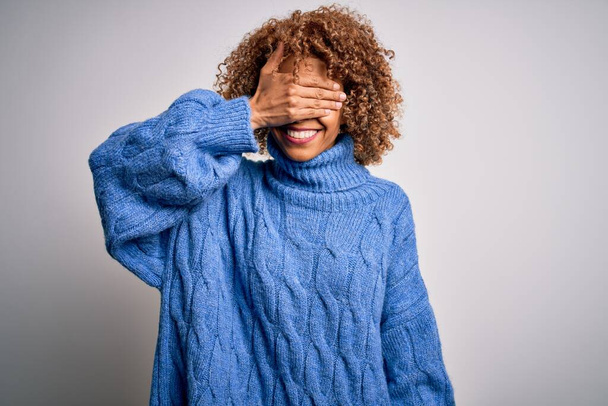 Young beautiful african american woman wearing turtleneck sweater over white background smiling and laughing with hand on face covering eyes for surprise. Blind concept. - Foto, Imagem
