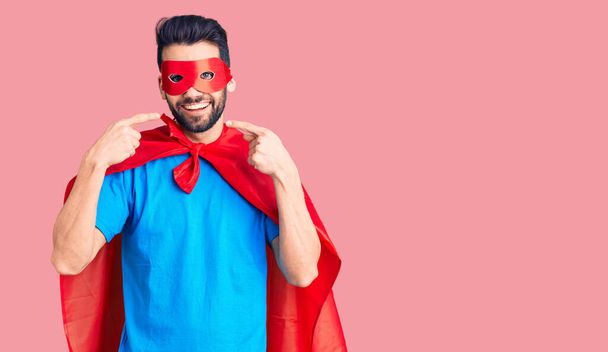 Young handsome man with beard wearing super hero costume smiling cheerful showing and pointing with fingers teeth and mouth. dental health concept.  - Photo, Image