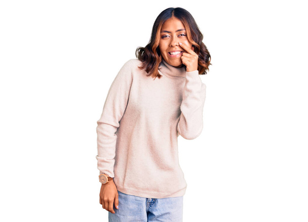 Young beautiful mixed race woman wearing winter turtleneck sweater pointing with hand finger to face and nose, smiling cheerful. beauty concept  - Foto, imagen