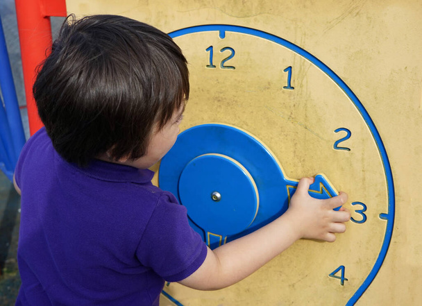 Çocuk yaz mevsiminde tahta saatle oyun sahasında zaman öğreniyor, çocuk saati söylemeyi öğreniyor, çocuk elleri, çocuk gelişimi için oynayarak öğrenme kavramı.   - Fotoğraf, Görsel