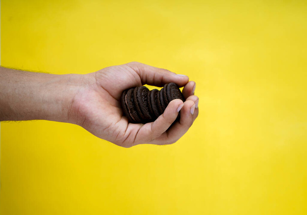 hands holding chocolate biscuits on a yellow background with copy space - Photo, Image