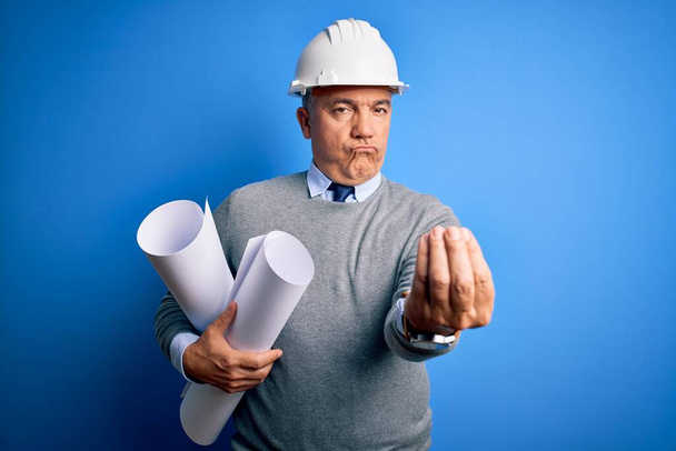 Middle age handsome grey-haired architect man wearing safety helmet holding blueprints doing money gesture with hands, asking for salary payment, millionaire business - Фото, изображение