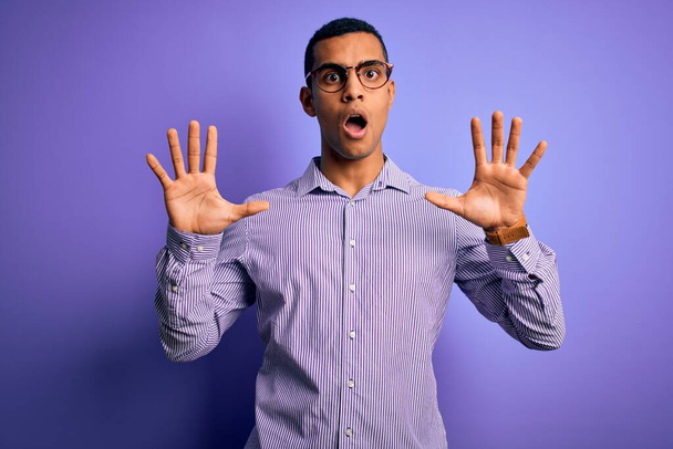 Handsome african american man wearing striped shirt and glasses over purple background doing stop gesture with hands palms, angry and frustration expression - Fotografie, Obrázek