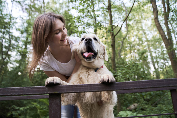 Happy woman with labrador standing on bridge among forest on summer day - Foto, immagini