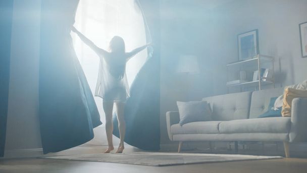 Beautiful Young Brunette Opens Curtains To let Morning Sunlight Into Cozy Living Room. Sensual Girl Rising Early and Greeting New Day. - Photo, image