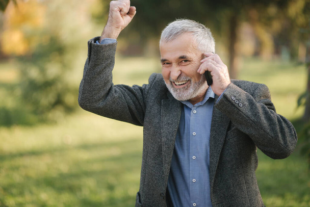 Mutlu yaşlı bir adam telefonda biriyle konuşur. Güzel sakallı yakışıklı adam gülümse ve neşelen - Fotoğraf, Görsel
